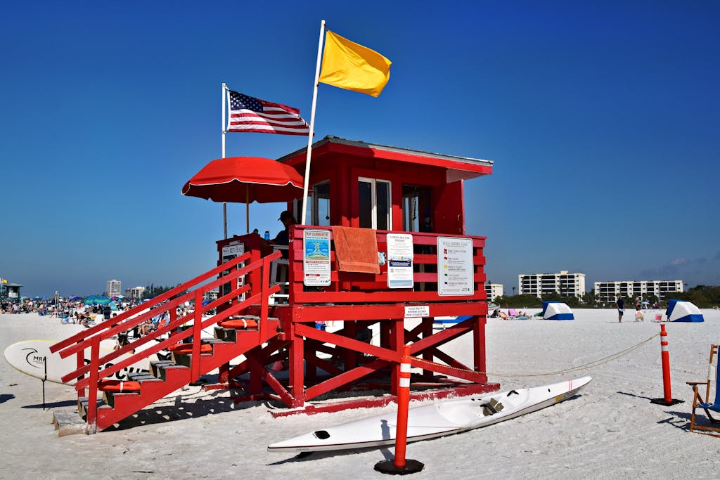 Bright red lifeguard tower with flags on a busy, sunlit beach, perfect for vacation scenery.