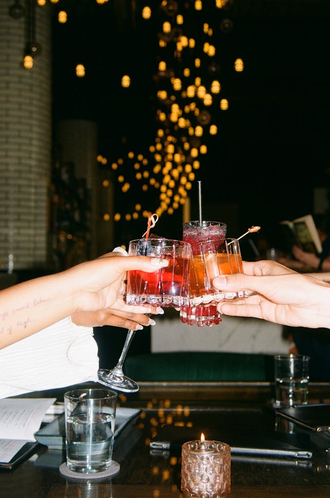 Friends raise colorful cocktails in a vibrant bar setting, celebrating casually.