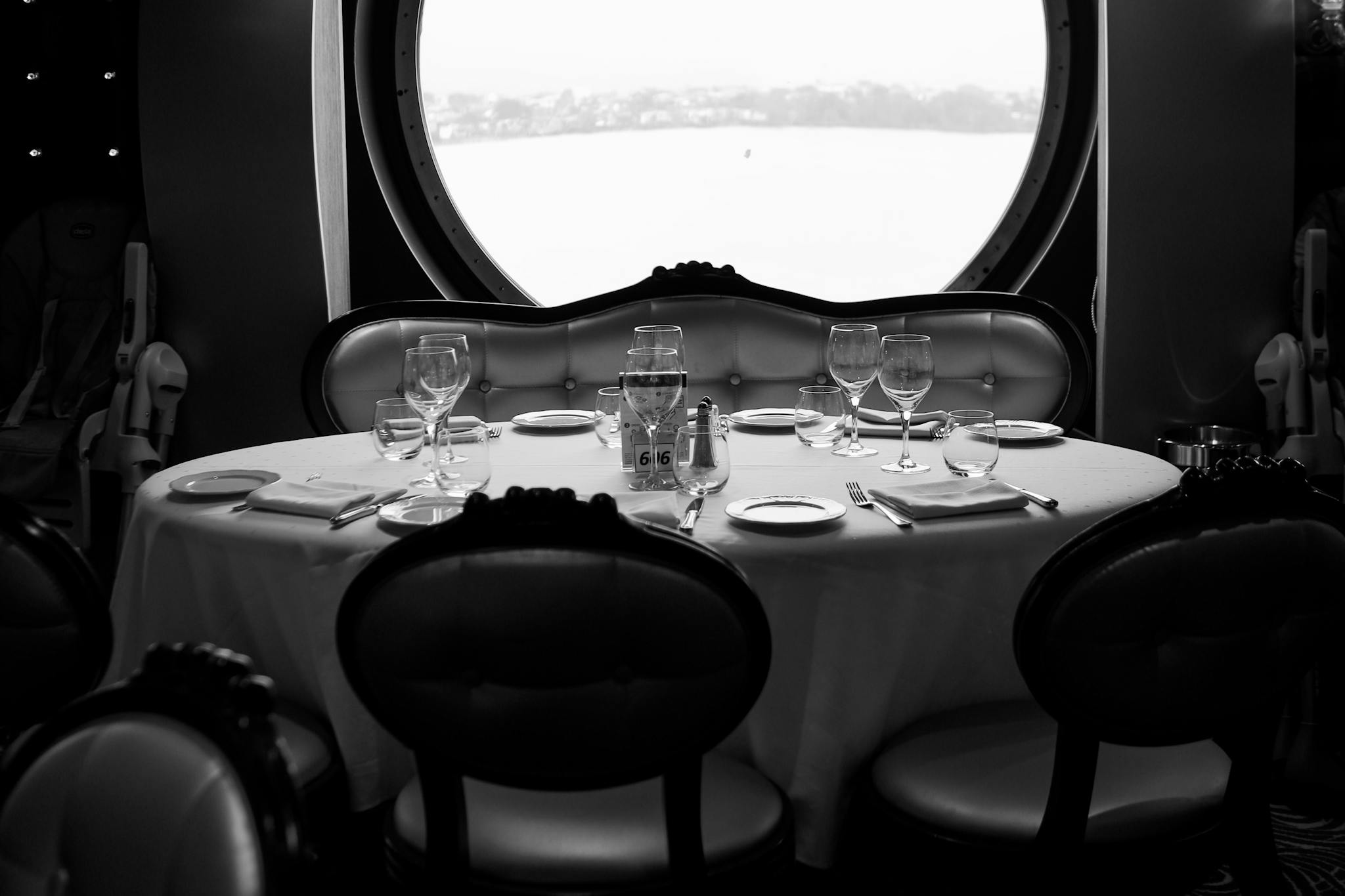 Luxury cruise ship dining room featuring a set table with an ocean view through a round window.